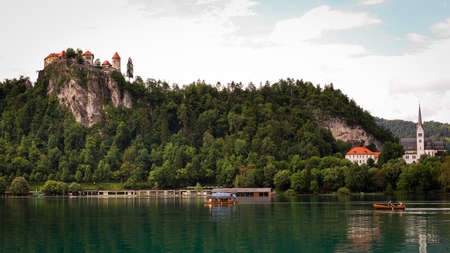 View of the Bled castle and church with boats on the lake in the foregroundの写真素材
