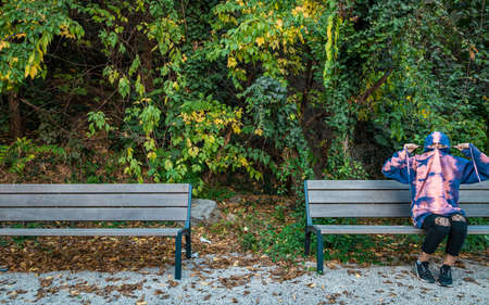 Young girl hiding in a hoodie on a bench in a park