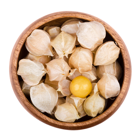 Physalis in a wooden bowl on white background. Edible ripe fruits of Physalis peruviana, a plant in the nightshade family. Light brown papery husks fully encloses the orange fruits. Isolated macro.の写真素材