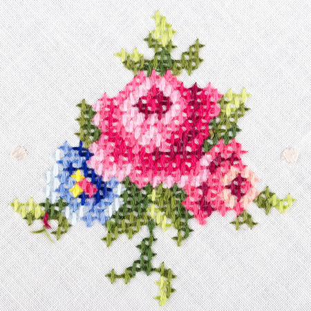 Rose motiv hand embroidery on white linen tablecloth.  Multicolored cross stich decoration with yarn. Handicraft. Macro photo close up from above.の写真素材