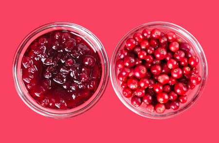 Lingonberry jam and lingonberries in glass bowls over pink. Fresh red fruits of Vaccinium vitis-idaea, also mountain cranberries, partridgeberries or cowberries. Staple food in Scandinavian cuisine.の写真素材