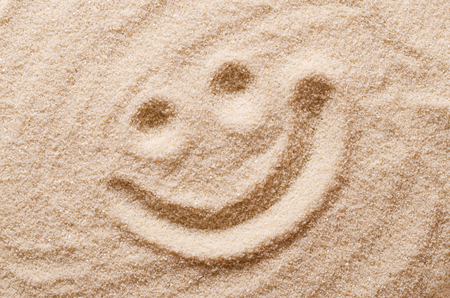 Happy smiling face in the sand. Eyes and mouth drawn with a finger in dry ocherous sand. Macro photo close up from above.の写真素材