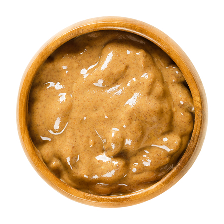 Almond butter in wooden bowl. Smooth brown food paste made of almonds. Puree of the nuts of Prunus dulcis. Isolated macro food photo close up from above on white background.の写真素材