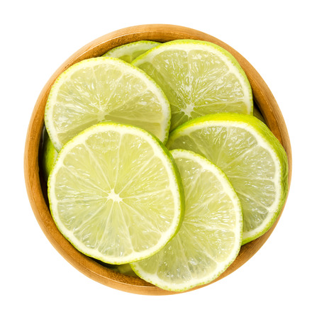 Lime slices in wooden bowl. Fresh cut unripe green edible citrus fruit discs. Key lime, Citrus...