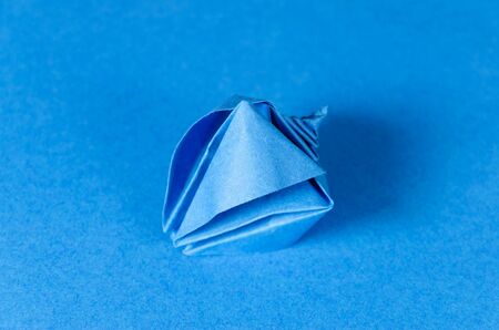 Blue origami seashell on blue background. Japanese art of paper folding. Flat square sheet of paper...