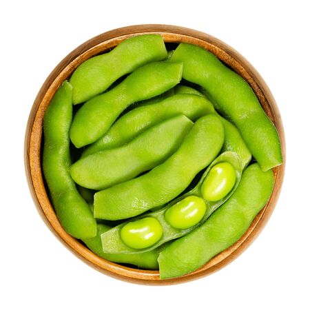 Green soybeans in the pod, edamame, in wooden bowl. Unripe soya beans, also Maodou. Glycine max, a legume, edible after cooking and rich protein source. Closeup, on white background, macro food photo.の写真素材