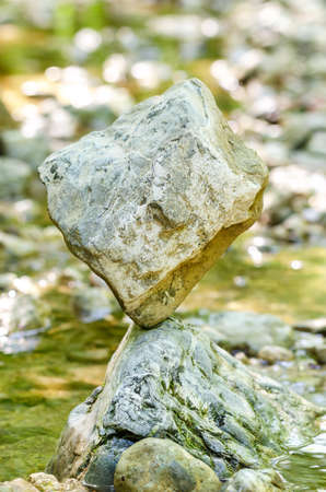 Balanced rock at the creek. A cube shaped rock is naturally balanced on top of a rock in a creek,...