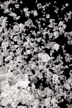 Sea salt, fleur de sel, close-up of crystals on a black surface. Also flor de sal, a salt that forms a thin, delicate crust on the sea water that evaporates. Finishing salt.の写真素材
