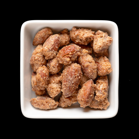 Candied almonds in a white square bowl. Homemade, in a special way cooked almonds, whole nuts coated in crunchy sugar. Sold at Christmas markets. Close-up, from above.の写真素材