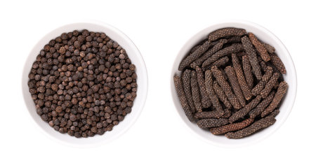Dried black peppercorns and long pepper catkins, in white bowls. Berries of Piper nigrum, and fruits...