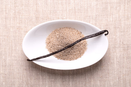 Vanilla bean and vanilla sugar, in white bowl, on linen cloth. Dried whole, dark brown, ripe fruit of Vanilla planifolia. Spice with distinctive flavor.の写真素材