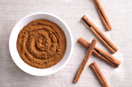 Cinnamon powder, in a white bowl on linen fabric. Raw bark of Indonesian cinnamon, Cinnamomum...