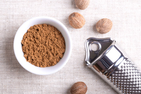 Nutmeg powder, ground nutmeg in a white bowl on linen fabric. Fragrant or true nutmeg, a spice, also...