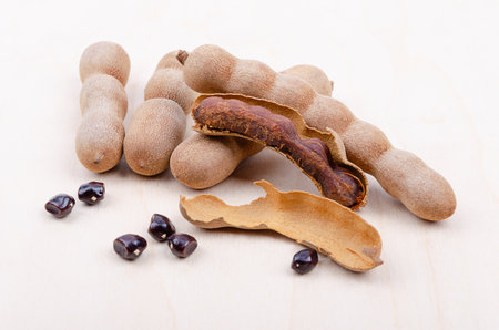 Tamarind fruits, whole, cracked open, and seeds on a light wooden board. Brown, pod-like fruits of Tamarindus indica, with sweet-sour flavor, typically enjoyed as a paste or candy.の写真素材