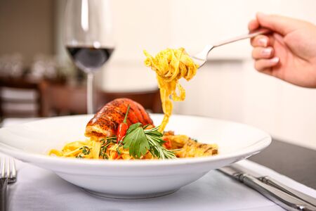 Close up of a plate pasta with shrimp. With a fork taking some pasta and a glass wine in background