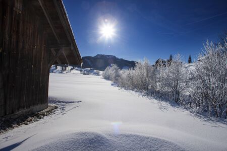 sun and blue sky on a cold day in the swiss mountains with snow landscape with sunset and treesの写真素材
