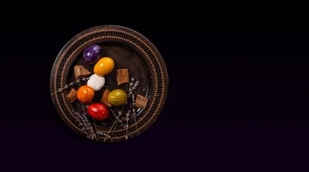 Colored easter Eggs in a plate with black background and copy space. With grass and flowersの写真素材