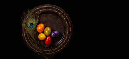 Colored easter Eggs in a plate with black background and copy space. With grass and flowersの写真素材