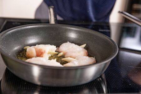 hands of cook preparing food in a frying pan with meat and vegetablesの写真素材