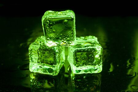Wet ice cubes on black background with green light.の写真素材