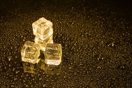 Ice cubes in yellow light on black wet table.の写真素材