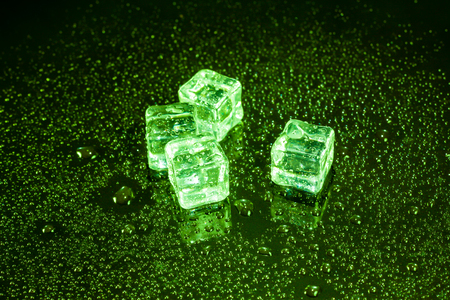 Ice cubes in green light on black wet table.の写真素材