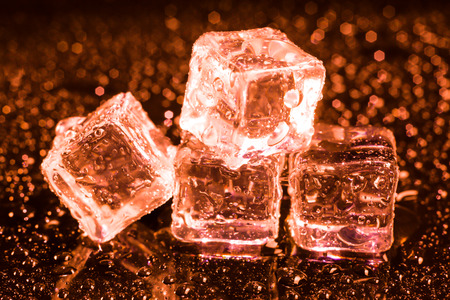 Ice cubes in red light on black wet table.の写真素材