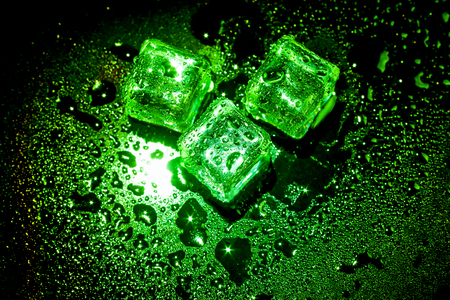 Green ice cubes on black wet table.の写真素材