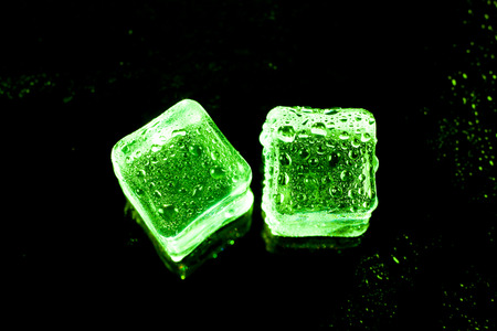 Green ice cubes on black wet table.の写真素材