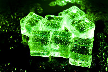 Green ice cubes on black wet table.の写真素材