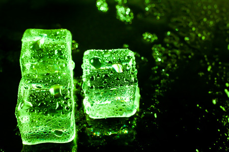 Green ice cubes on black wet table.の写真素材