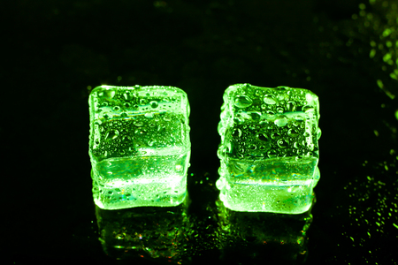 Green ice cubes on black wet table.の写真素材