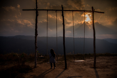 Lonely woman watching sunset alone sitting on swings on the mountain at sunset.