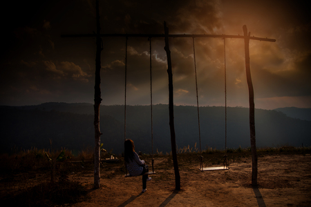 Lonely woman watching sunset alone sitting on swings on the mountain at sunset.の写真素材
