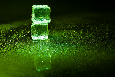 Green ice cubes reflection on black table.の写真素材