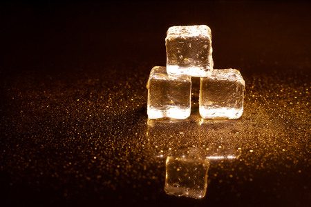 Golden ice cubes reflection on black table.の写真素材