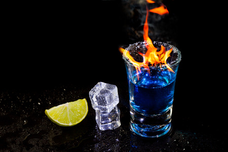 Cocktail blue burning in shot glass  with salt and lime, ice cubes on black background.の写真素材