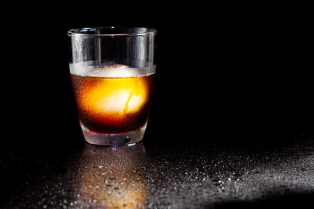 Cold americano decoration with ice ball in whisky glass on a black table.