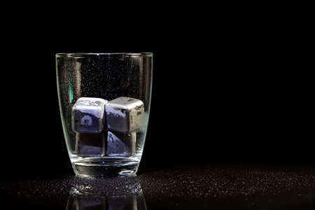 stainless steel cubes simulating ice in whisky glass on a black table.の写真素材