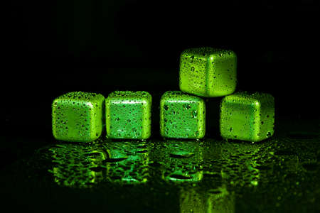 Green stainless steel cubes simulating ice for cooling drinks on a black surface with a reflection.の写真素材
