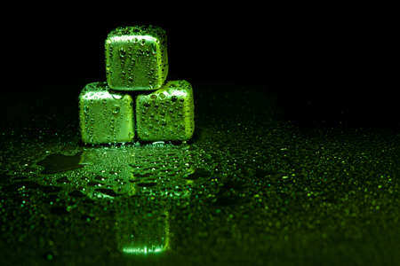 Green stainless steel cubes simulating ice for cooling drinks on a black surface with a reflection.の写真素材