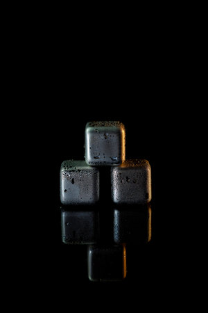 Stainless steel cubes simulating ice for cooling drinks on a black surface with a reflection.の写真素材