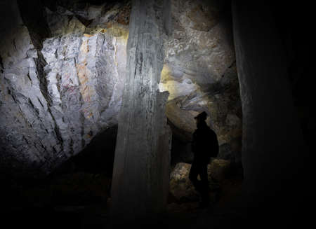 Hiker exploring dark cave illuminating it by headlamp only. Shot in Canadian Rockies on Kananaskis Ice Cave Trail, Alberta, Canadaの写真素材