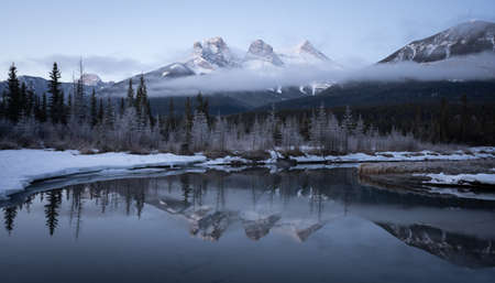 Winter pre-sunrise shot from Canadian Rockies with mountain reflected in water, shot at Three Sisters Mountain, Canmore, Alberta, Canadaの写真素材