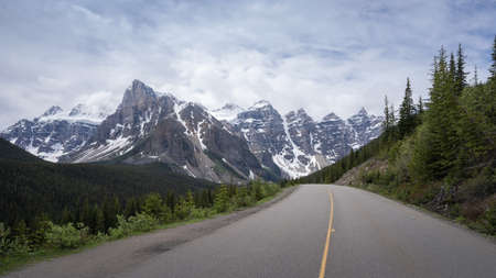 Asphalt road leading through beautiful alpine valley, shot on a overcast day at Moraine Lake road,...