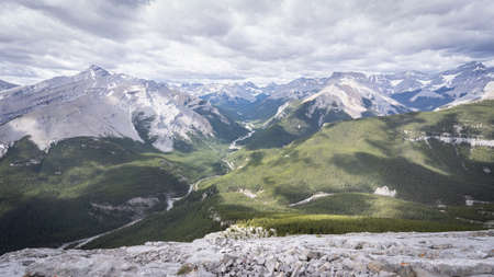 View on beautiful alpine valley from mountain summit with dramatic cloudy sky, shot during summer day at Nihahi Ridge, Kananaskis, Alberta, Canadaの写真素材
