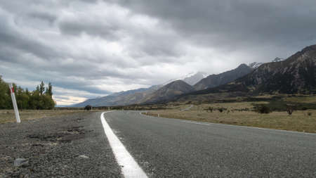 Road leading towards mountains, with cloudy sky. Low perspective shot made in Aoraki Mt Cook...