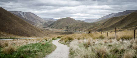 Panorama of dry valley with path leading to the centre of frame. Shot on overcast day in Lindis Pass, New Zealandの写真素材