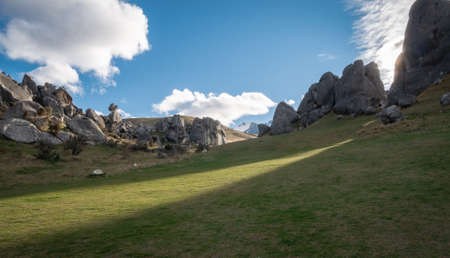 Sun setting behind unusually shaped rocks and sheding rays of lights on green grass in front of them. Beautiful Stonehengelike landscapes vistaの写真素材