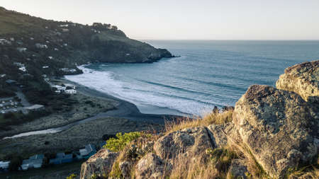 Late afternoon, sunset shot of small bay surrounded by hills with rocks in foregroundの写真素材